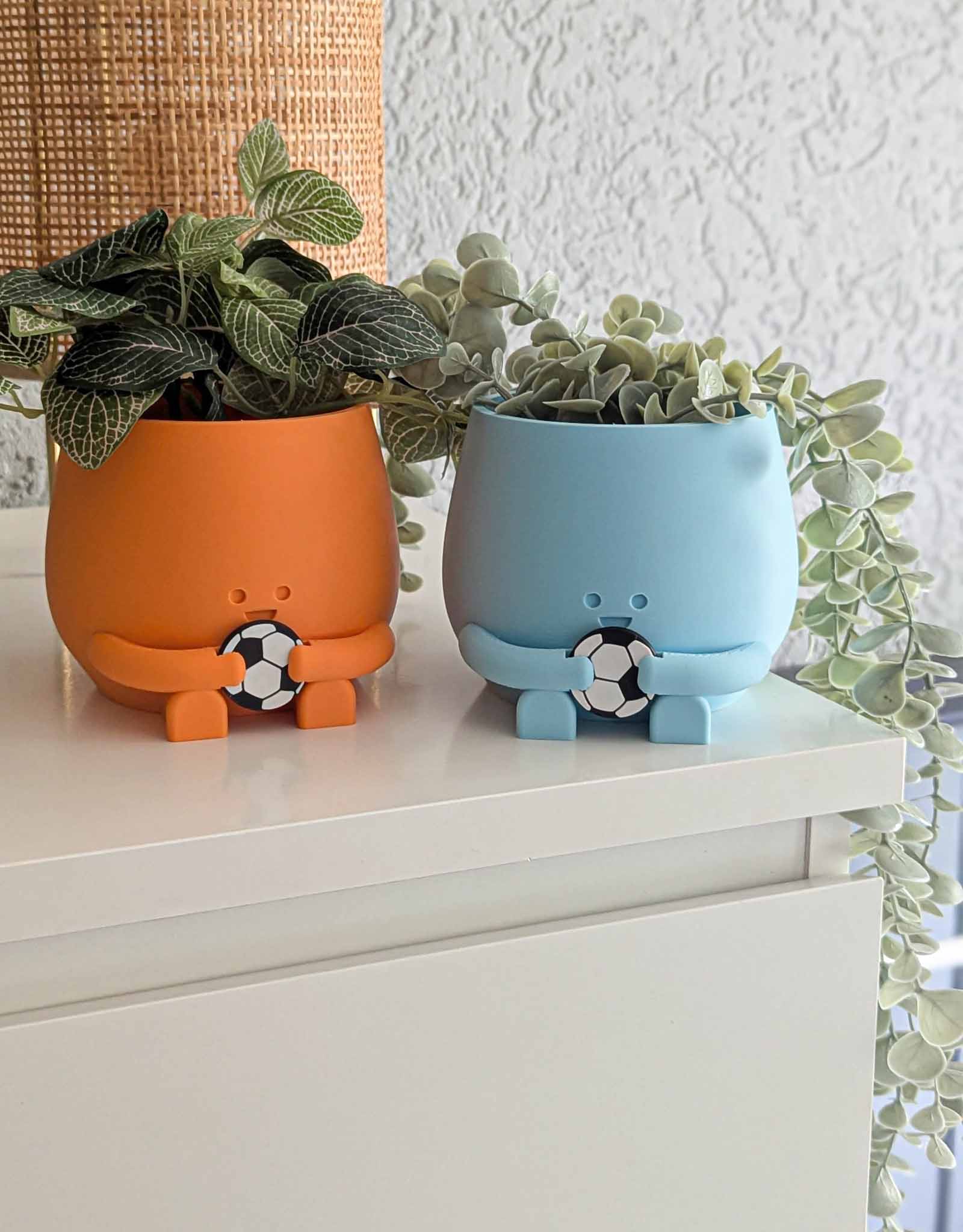 Two happy plant pots in orange and light blue both holding a football